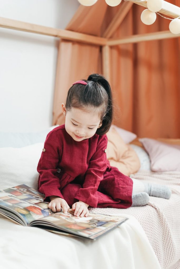 girl in red dress sitting on bed reading book